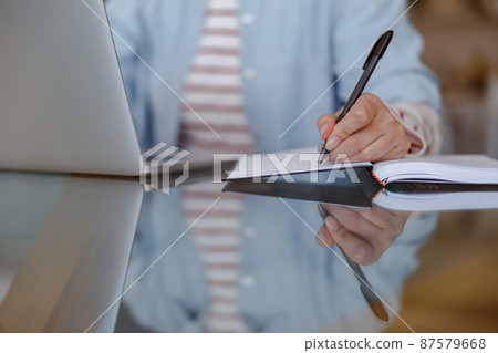 Woman using laptop and writing in notebook at home 87579668