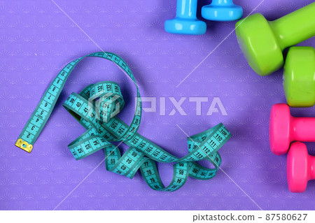 Dumbbells and measure tape in cyan color on purple texture 87580627