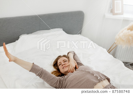 Beautiful woman wakes up in her bed, smiles and stretches Beautiful woman wakes up in her bed, smiles and stretches 87580748