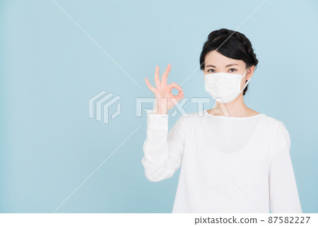 A woman wearing a white blouse wearing a mask and giving an OK sign A woman wearing a white blouse wearing a mask and giving an OK sign 87582227