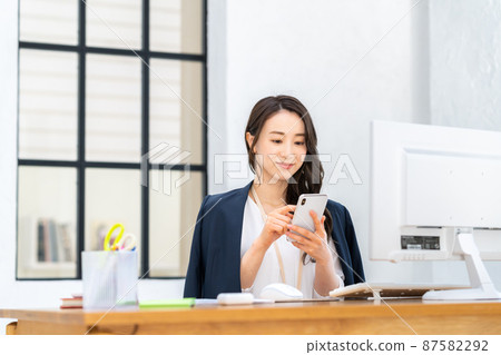 A young business woman looking at a smartphone in the office A young business woman looking at a smartphone in the office 87582292
