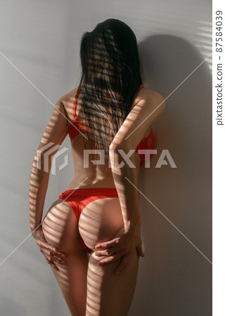 Young brunette woman in red lingerie posing in a sunshine Young brunette woman in red lingerie posing in a sunshine 87584039