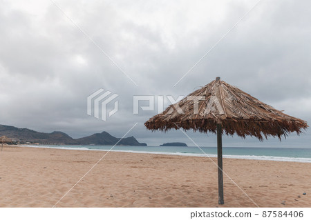 Wooden umbrella is on an empty beach 87584406
