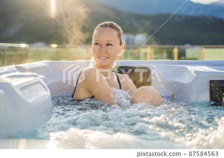 Portrait of young carefree happy smiling woman relaxing at hot tub during enjoying happy traveling moment vacation life against the background of green big mountains 87584563