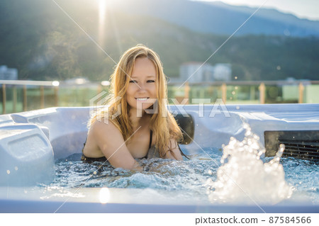 Portrait of young carefree happy smiling woman relaxing at hot tub during enjoying happy traveling moment vacation life against the background of green big mountains 87584566