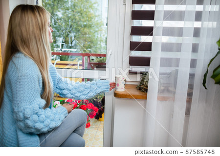 The girl puts the cup down on the windowsill and looks out the window. The girl puts the cup down on the windowsill and looks out the window. 87585748