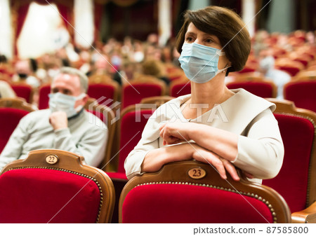 mature woman in antivirus mask watching play in the theater mature woman in antivirus mask watching play in the theater 87585800