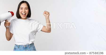 Happy asian woman shouting at megaphone, making announcement, advertising something, standing over white background 87588196