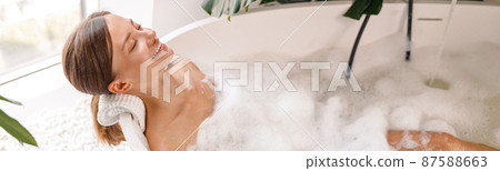 Relaxed woman looking happy while taking bubble bath in her beautiful bathroom decorated with plants 87588663