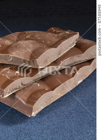 Piece of dark chocolate rests upon turn blue table Piece of dark chocolate rests upon turn blue table 87588948