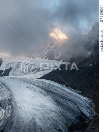 Twilight Mountains. Light on the glacier. Majestic glacier is illuminated by the bright golden evening sun. Vertical view. Big Aktru Glacier, Altai Mountains. 87589064