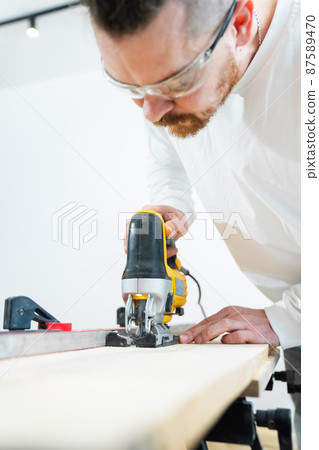 carpenter in protective gloves and glasses cuts wood with electric jigsaw carpenter in protective gloves and glasses cuts wood with electric jigsaw 87589470