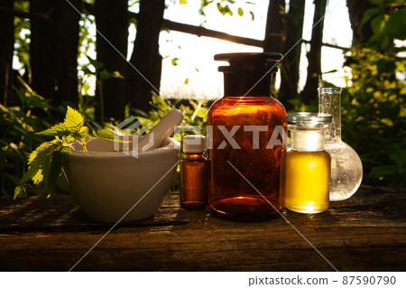 Phytotherapy - nettle in a mortar in the forrest. Bottles with herbal extracts on wood. 87590790