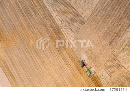 Aerial View. Tractor Plowing Field. Beginning Of Agricultural Spring Season. Cultivator Pulled By A Tractor In Countryside Rural Field Landscape 87591354