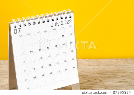 July 2022 desk calendar on wooden table with yellow background. 87595554