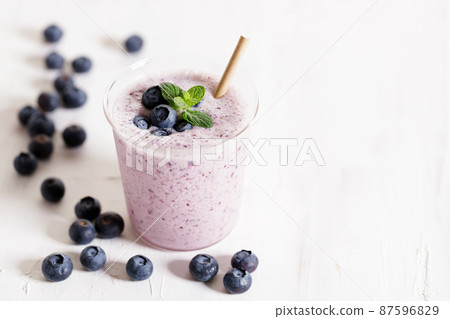 Glass of blueberry milkshake with fresh blueberries on white wooden background. 87596829