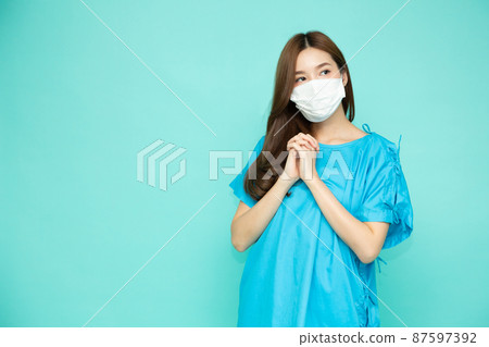 Asian girl in patient suit wearing white face mask and feeling hopeful isolated on green studio background Asian girl in patient suit wearing white face mask and feeling hopeful isolated on green studio background 87597392