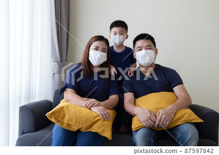 Asian family wearing protective medical mask for prevent virus Covid-19 and sitting together in living room. Family protection from contaminated air concept 87597842
