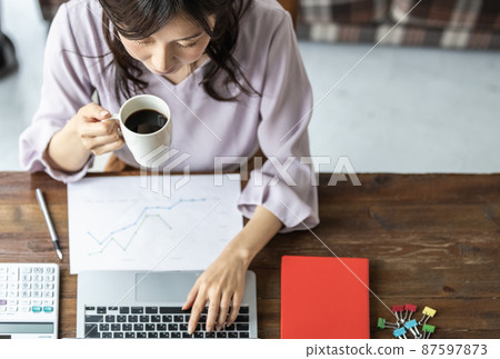 辦公桌上拿著杯子工作的女商人 87597873