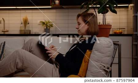 A talented and creative artist draws a picture with a pen on a tablet while sitting comfortably on the sofa in the living room. A talented and creative artist draws a picture with a pen on a tablet while sitting comfortably on the sofa in the living room. 87597904