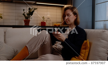 Natural girl artist draws on a digital tablet while sitting on a comfortable sofa in the living room Natural girl artist draws on a digital tablet while sitting on a comfortable sofa in the living room 87597907