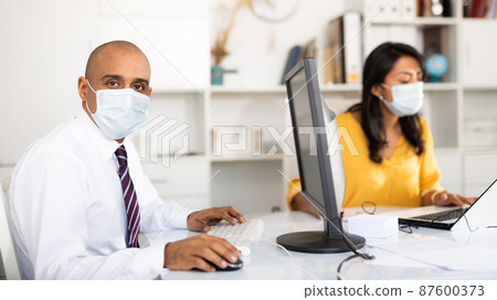Director and secretary in protective medical masks work in office Director and secretary in protective medical masks work in office 87600373