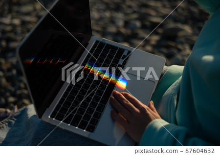 A woman is typing on a laptop. Rainbow light from a prism. A woman is typing on a laptop. Rainbow light from a prism. 87604632