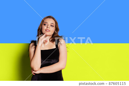 Portrait of young beautiful girl with dreamy and thoughtful facial epression isolated over blue and yellow ukrainian flag background Portrait of young beautiful girl with dreamy and thoughtful facial epression isolated over blue and yellow ukrainian flag background 87605115