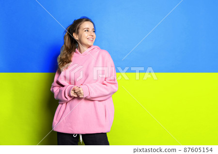 Portrait of young beautiful woman in pink hoodie cheerfully smiling isolated over blue and yellow ukrainian flag background 87605154