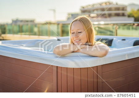Portrait of young carefree happy smiling woman relaxing at hot tub during enjoying happy traveling moment vacation life against the background of green big mountains 87605451