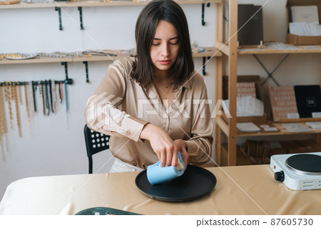 Portrait of focused young woman artisan taking out beautiful white piece of author candle of silicone mold. Process of making handmade natural candle at workshop. 87605730