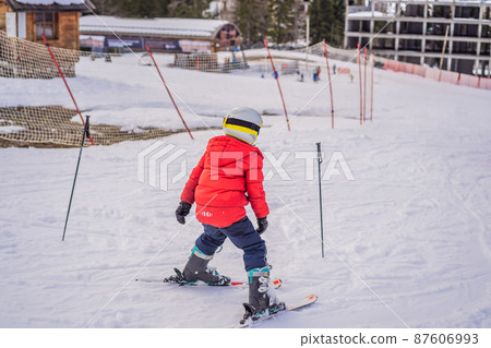 Child skiing in mountains. Active toddler kid with safety helmet, goggles and poles. Ski race for young children. Winter sport for family. Kids ski lesson in alpine school. Little skier racing in snow Child skiing in mountains. Active toddler kid with safety helmet, goggles and poles. Ski race for young children. Winter sport for family. Kids ski lesson in alpine school. Little skier racing in snow 87606993