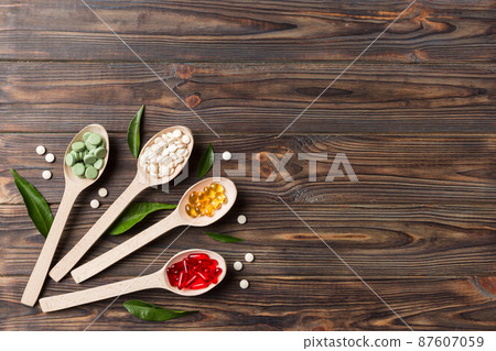 Top view Variety of vitamin and mineral pills in wooden spoon on Colored background. Top view of assorted pharmaceutical medicine pills. Dietary supplement healthcare product Top view Variety of vitamin and mineral pills in wooden spoon on Colored background. Top view of assorted pharmaceutical medicine pills. Dietary supplement healthcare product 87607059