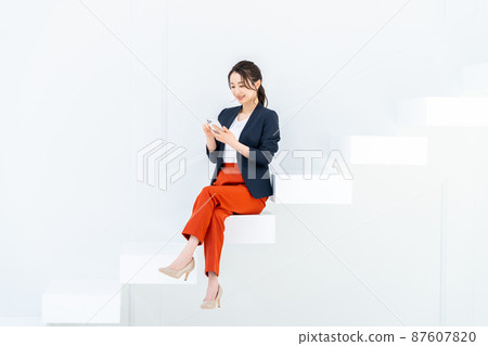 Business woman looking at a smartphone on the stairs Business woman looking at a smartphone on the stairs 87607820