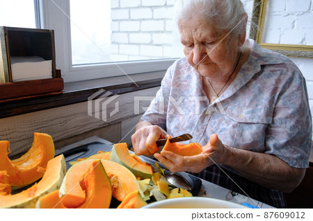 Old woman cuts and pills yellow pumpkin, cooking pumpkin soup, retirement life, selective focus Old woman cuts and pills yellow pumpkin, cooking pumpkin soup, retirement life, selective focus 87609012