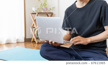 A man doing yoga stretching while watching a video on a PC A man doing yoga stretching while watching a video on a PC 87611985