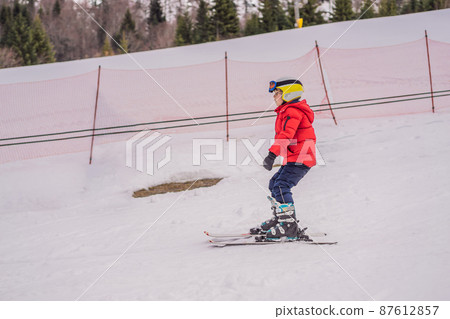 Child skiing in mountains. Active toddler kid with safety helmet, goggles and poles. Ski race for young children. Winter sport for family. Kids ski lesson in alpine school. Little skier racing in snow Child skiing in mountains. Active toddler kid with safety helmet, goggles and poles. Ski race for young children. Winter sport for family. Kids ski lesson in alpine school. Little skier racing in snow 87612857