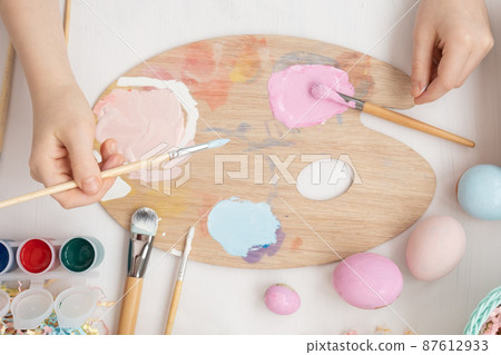 Preparation for Easter. The child is holding a large egg in his hands. Pastel shades on the palette. A child's hand paints an egg light blue with a brush. Happy Easter 87612933