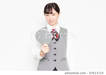 Business woman standing in front of a white background and checking her skin with a hand mirror Business woman standing in front of a white background and checking her skin with a hand mirror 87613724