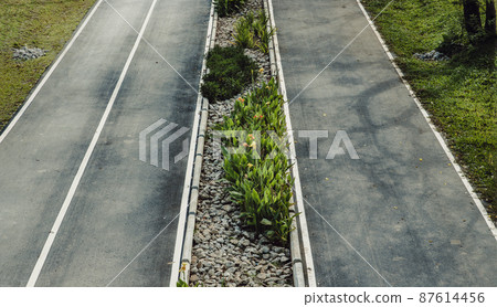 Top view of empty road texture with median strip in the middle surrounded green grass. 87614456