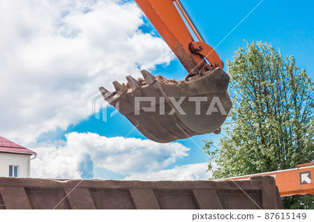 Excavation works. The bucket of the tractor loads the soil with a shovel into the back of a dump truck on the construction site 87615149