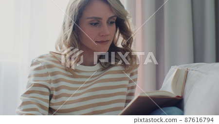 Smiling young pretty woman reading book while sitting on sofa at home. Nice to spend free time on the weekend. Smiling young pretty woman reading book while sitting on sofa at home. Nice to spend free time on the weekend. 87616794