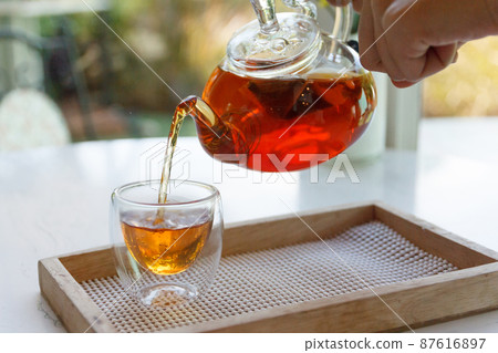 Close up of the hand pouring green tea from glass kettle to small cup Close up of the hand pouring green tea from glass kettle to small cup 87616897