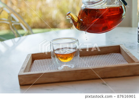Hot green tea is poured from the kettle into a small cup 87616901