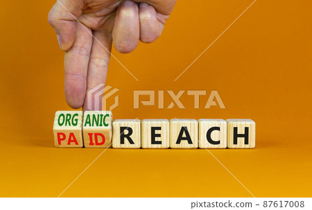 Organic or paid reach symbol. Businessman turns wooden cubes and changes words paid reach to organic reach. Beautiful orange table orange background copy space. Business organic or paid reach concept. 87617008