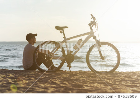 male cyclist is resting sitting on a sandy beach . male cyclist is resting sitting on a sandy beach . 87618609