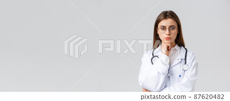 Healthcare workers, medicine, insurance and covid-19 pandemic concept. Serious smart, professional female doctor in glasses and white scrubs, thinking, taking decision or choice, look camera 87620482