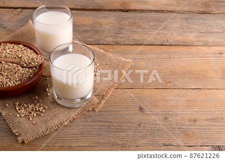 Vegan non diary buckwheat milk in glasses with buckwheat groats in a clay bowl on a wooden background. 87621226