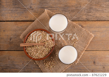 Vegan non diary buckwheat milk in glasses with buckwheat groats in a clay bowl on a wooden table. Vegan non diary buckwheat milk in glasses with buckwheat groats in a clay bowl on a wooden table. 87621229