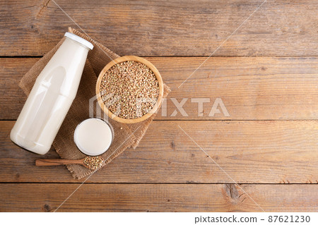 Vegan non diary buckwheat milk in bottle with buckwheat groats on a wooden background. Vegan non diary buckwheat milk in bottle with buckwheat groats on a wooden background. 87621230